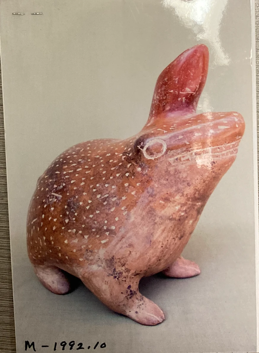 A photograph of a red clay horned frog with white speckles and a pointed horn, labeled M-1992.10.